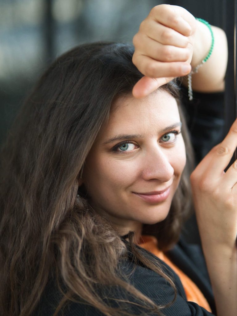 Junge Frau mit langen Haaren zeigt Daumen hoch und lächelt freundlich.